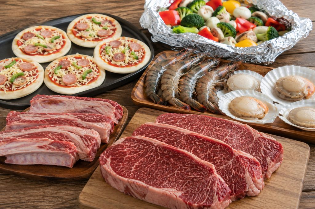 焼く前の厚切りステーキ、海鮮、野菜のホイル焼き、ピザが並べられている様子