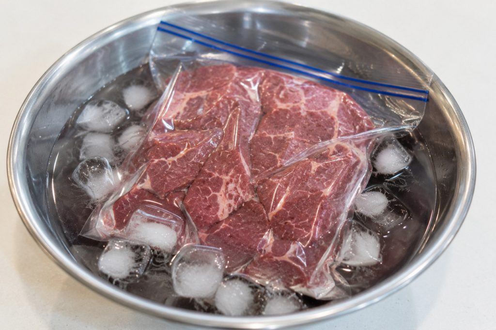 氷水が入ったボウルで冷凍肉が解凍されている様子