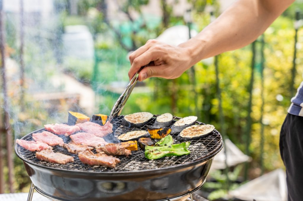 庭のバーベキューコンロで肉と野菜を焼いている様子