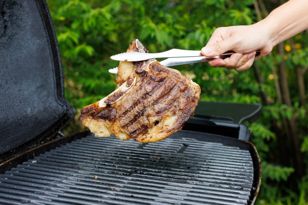 バーベキューグリルで焼いている骨付き肉をトングで持ち上げている