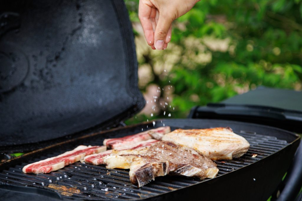 バーベキューグリルで焼いている骨付き肉に塩をかけている